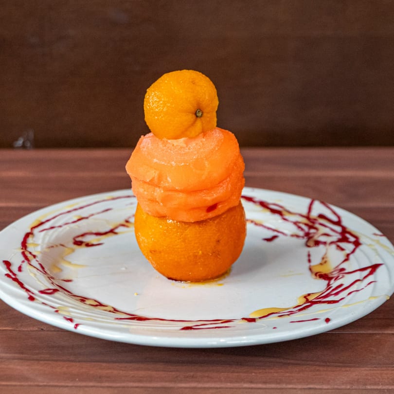 Stacked orange dessert with sorbet and fruit, drizzled with red and yellow sauces on a white plate.