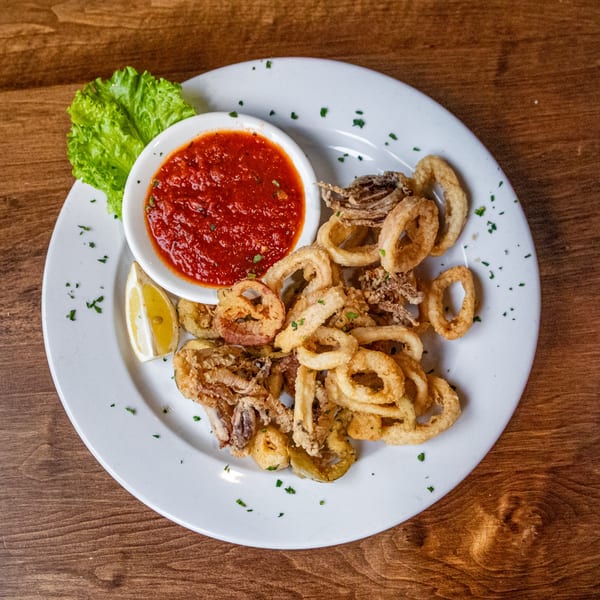 Crispy fried calamari with a side of red marinara sauce, lemon wedge, and lettuce on a white plate.