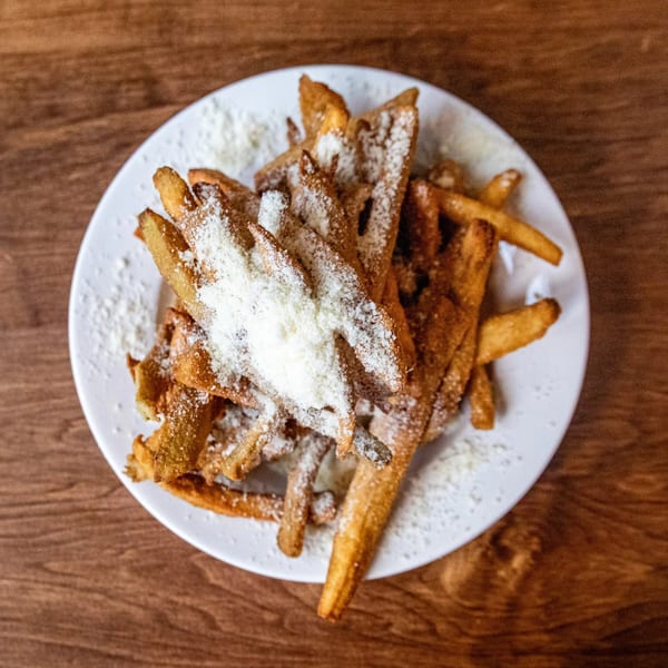 A white plate filled with golden-brown french fries, generously sprinkled with grated Parmesan cheese.