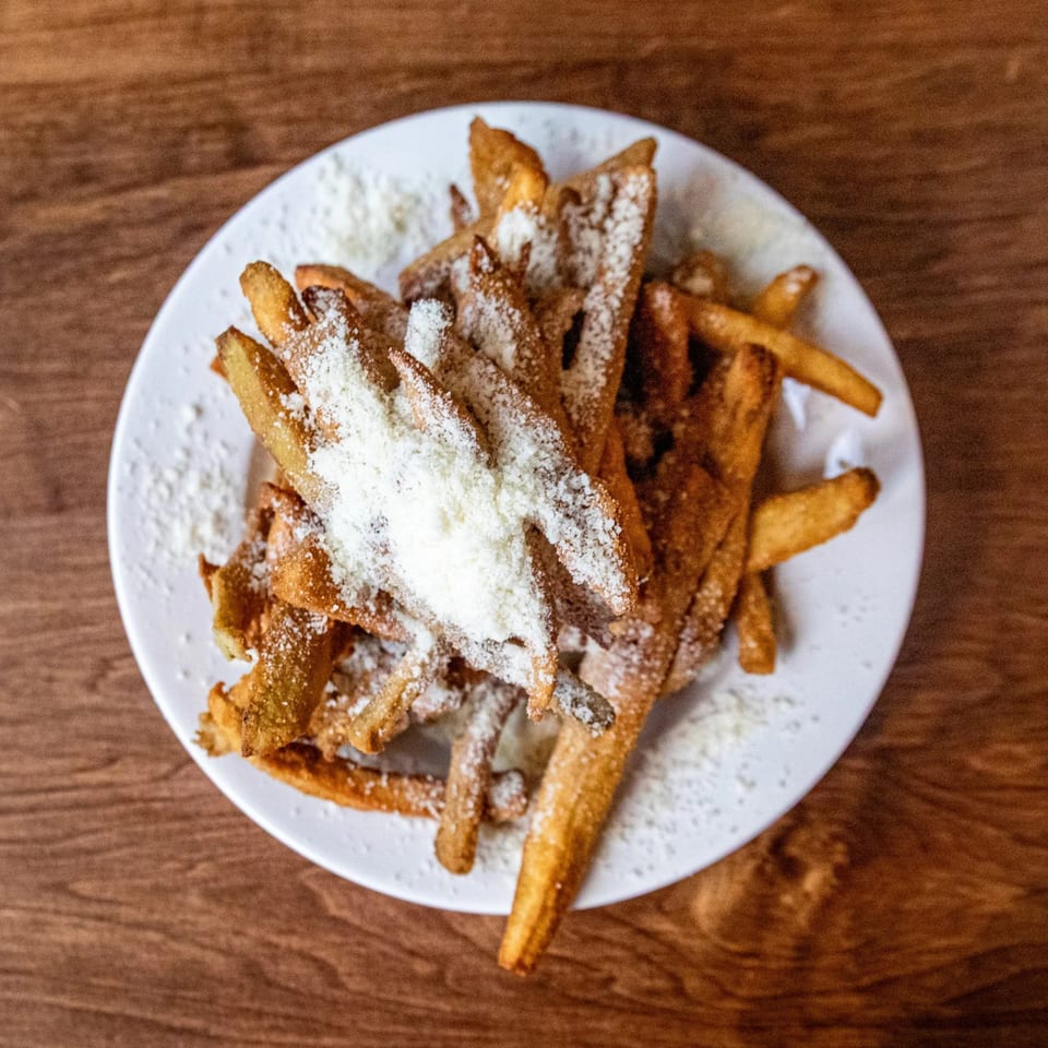 A white plate filled with golden-brown french fries, generously sprinkled with grated Parmesan cheese.