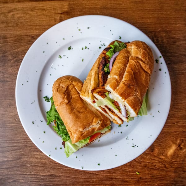 Two halves of a grilled chicken sandwich with lettuce, tomato, and red onion on a white plate.