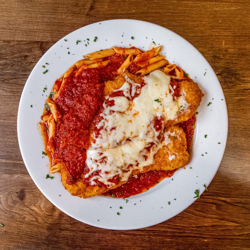 Cafe Pesto's chicken parmesan with penne pasta and marinara sauce on a white plate.